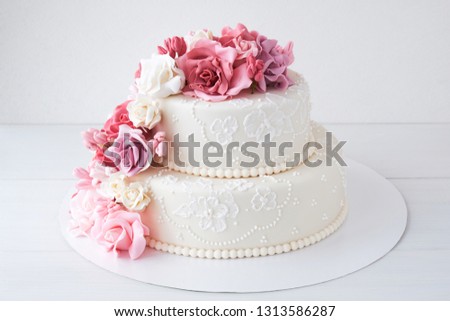 Two-tiered white wedding cake decorated with pink flowers on a white wooden background.