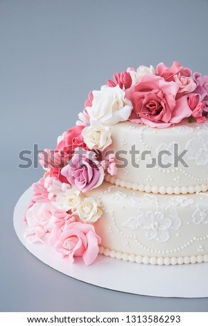 Two-tiered white wedding cake decorated with pink flowers on a gray background. Cutout.