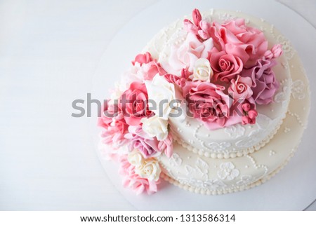 Wedding cake decorated with pink flowers on a white wooden background. Top view.