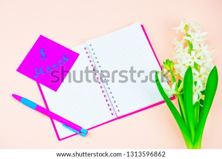 Festive concept. Spring Flowers and Women's Day Greetings. White hyacinth on a gentle background, next to a notebook in a pink cover and a bright ballpoint pen. A green sticker with the signature Marc