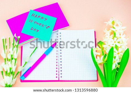 Festive concept. Spring Flowers and Women's Day Greetings. White hyacinth on a gentle background, next to an open notebook in a pink cover, a bright ballpoint pen and a pack of stickers. On one green 
