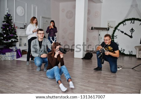 The team of two photographers shooting on studio behind another three workers. Professional photographer on work. One of them joking and holds horns over head.
