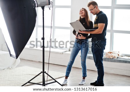 Photographer explaining about the shot to his assistant in the studio and looking on laptop. Teamwork and brainstorm.