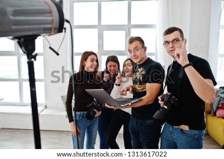Photographer explaining about the shot to his team in the studio and looking on laptop. Talking to his assistants holding a camera during a photo shoot. Teamwork and brainstorm.