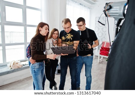 Photographer explaining about the shot to his team in the studio and looking on laptop. Talking to his assistants holding a camera during a photo shoot. Teamwork and brainstorm.