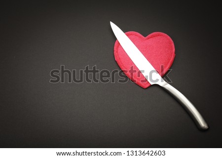 Sharp steel knife  above red heart like symbol about dangers situation for heard isolated on black background with copy space