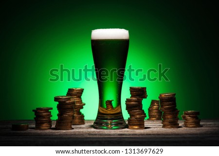 glass of irish ale standing on wooden table near golden coins on green background