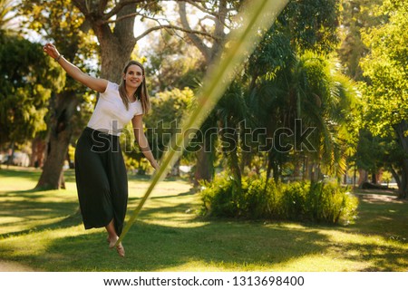 Woman balancing her walk on a loose rope tied between two trees. Woman practicing slack rope walking in a park. Royalty-Free Stock Photo #1313698400