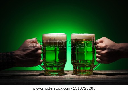 cropped view of men holding glasses of ale on green background