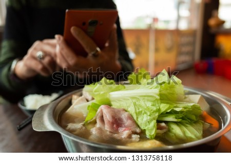 woman take a picture on hot pot with vegetables and pork
