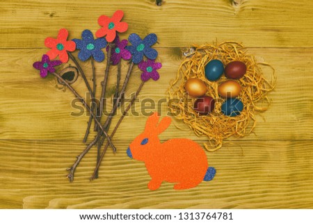 Painted Easter eggs in straw with flowers and bunny on wooden table.Toned photo.