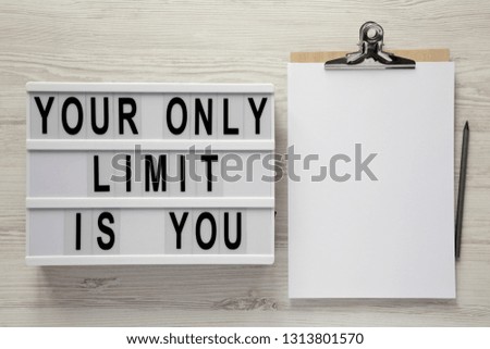 Lightbox with text 'Your only limit is you', clipboard on a white wooden surface, top view. From above, flat lay, overhead. 
