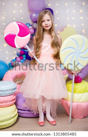 portrait of cute little girl holding huge lollipops with giant donuts and cupcakes decorations