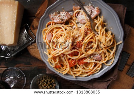 Spaghetti with chunks of fresh tuna, tomato and capers on a dark background