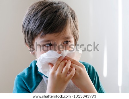Sick kid blowing nose into tissue, Unhealthy child suffering from running nose or sneezing and covering his nose and mouth, A boy catches a cold when season change, childhood wiping nose with tissue