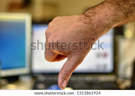 Male hand of Caucasian man makes thumbs down gesture. Indistinguishable blurred background of an office.