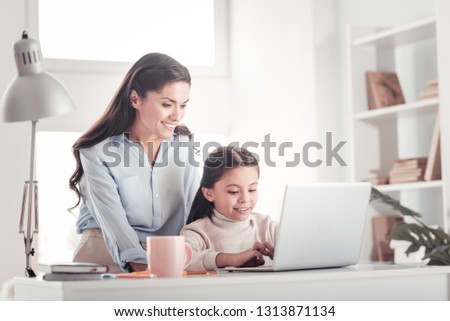 Enjoyable motherhood. Pretty young mother smiling while spending unforgettable family time playing computer games with daughter