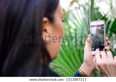 Over shoulder view of unrecognizable woman taking picture with smartphone in beautiful botanical garden indoor. Botanical green garden full of greenery. happy, blur, clean, bright, modern, colorful.