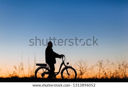 Active pension. Male cyclist on the e-bike or electric bicycle on the sunset background. Silhouette of the old man in profile. Travel. Sport.