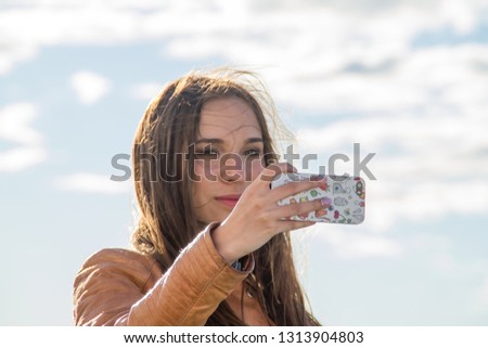 Young beautiful girl makes selfie against the background of clouds