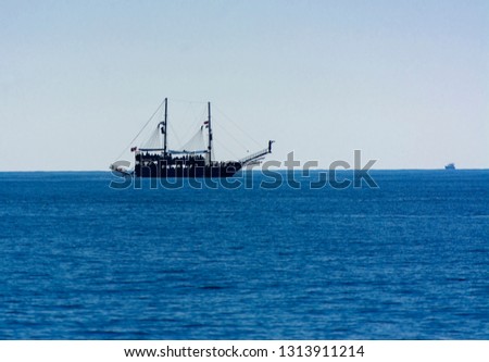 A large sailing ship in a pirate style in the open sea against a blue sky. Photos of the ship from the sea. The concept of summer holidays, sports, tourism