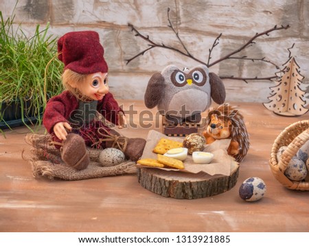Dreamlike card with toy characters. Three friends Lesovik, an owl and a hedgehog settled down with a lunch of eggs and cracker biscuits on forest hemp.