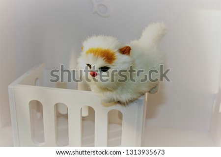 A small toy white kitten sits on a toy white cot in a children's house. Shabby Chic Style  in the interior of the children's room.