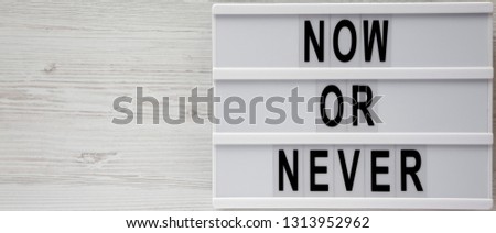 Lightbox with text 'Now or never' word on modern board on a white wooden background, top view. Copy space.