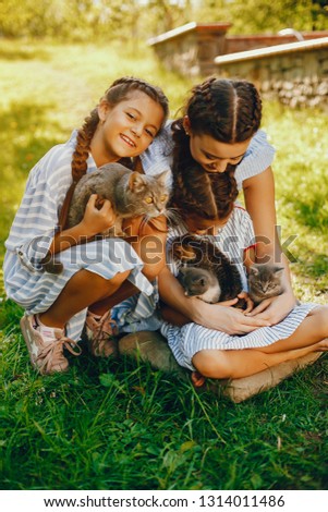 three beautiful and cute girls in blue dresses with beautiful hairstyles and make-up sitting in a sunny green garden and playing with a cats