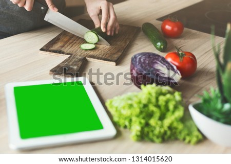 Digital tablet with chrome key screen on kitchen table, female hands cutting vegetables