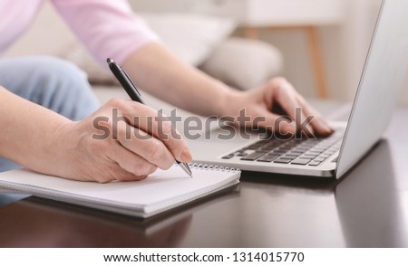 Creative process of making new text. Senior woman life or business coach writing down thoughts, ideas in copybook and working on laptop, closeup