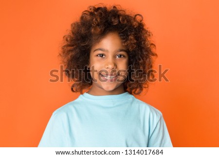 Portrait of adorable african-american child girl smiling to camera over orange background