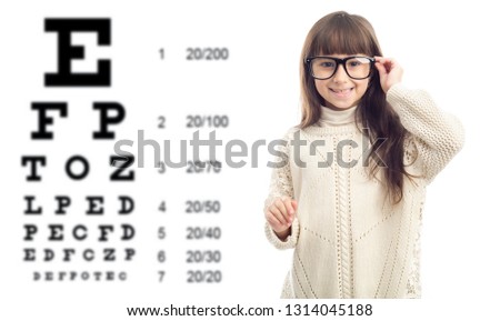 Little girl on the background vision test tables. Visit a doctor ophthalmologist. Portrait of cheerful girl 7 years old wearing glasses against eye chart in clinic.