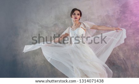 Beautiful and stylish bride in wedding dress with a lush flying skirt in Studio on grey textured background