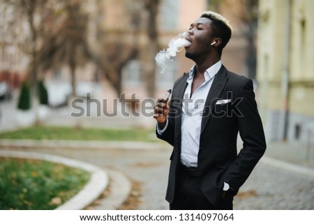 Handsome afro american business man with e-cigarette with smoke cloude standing on the city street