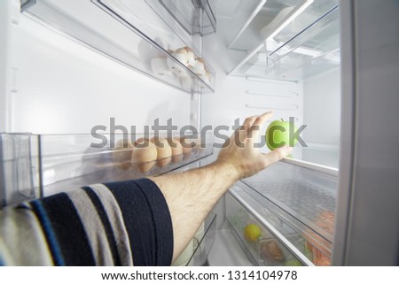 Hand reaching for a green apple in an open refrigerator