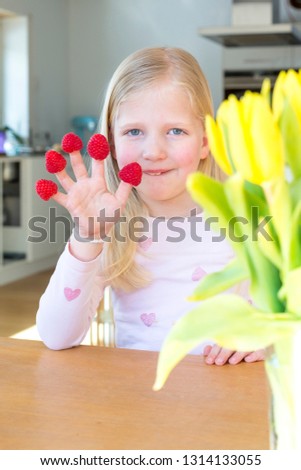 Portrait of blonde girl smiling with red raspberries on her fingers