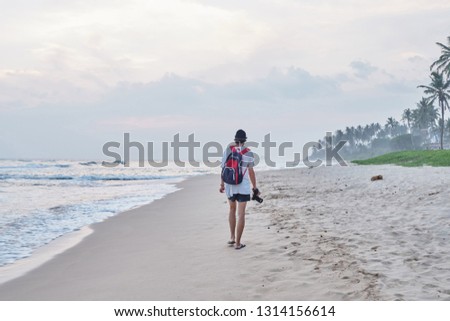 A young man walks along the beach, looks at the ocean and takes pictures. Sri-Lanka.