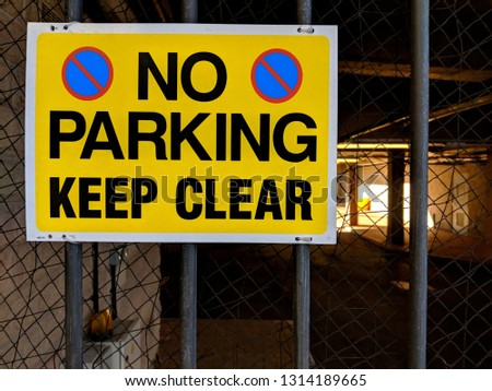 High visibility yellow and black 'No Parking Keep Clear' sign attached to iron bars on the gate of a secure parking lot