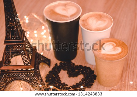A heart made out of coffee gains on the wooden table background between Eiffel tower toy and coffee takeaway cups. A gift for your couple on Valentines day concept. Latte art with a symbol of love.  