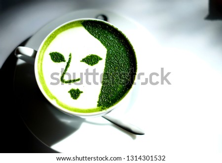 The iconic Japanese green tea latte with girl face on top made from green tea powder with the white cup on the plate with tea spoon and the shadow of cup from sun light.