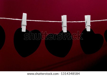 Black paper hearts with copy space hanging on white rope and attached with white laundry pins on dark red background