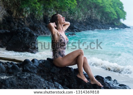 beautiful long-haired tanned girl of European appearance posing for the camera on the background of the ocean beach, stones and trees. Indonesia, Bali