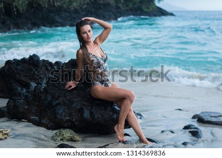 beautiful long-haired tanned girl of European appearance posing for the camera on the background of the ocean beach, stones and trees. Indonesia, Bali