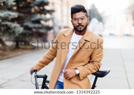 Bearded young hipster indian man posing next to his bicycle.