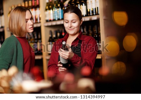 Picture of two women on blurred background of shelves with bottles of wine