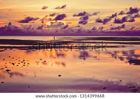 Lone fisherman in distance during beautiful reflected sunset with dramatic clouds in Maldives