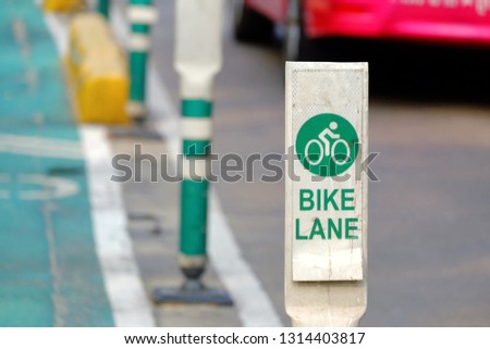 A bicycle lane sign on the white board at urban street area with blurred a car driving on the road 