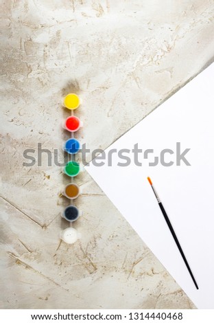 Flatlay with bright paints in small round containers, brush and white sheet of paper on grey cement backcground, Workspace, Artist, drawing, Hobby, Art, minimal, vertical