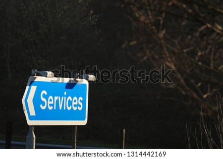 Blue motorway services arrow with dark background sign besides service station entrance